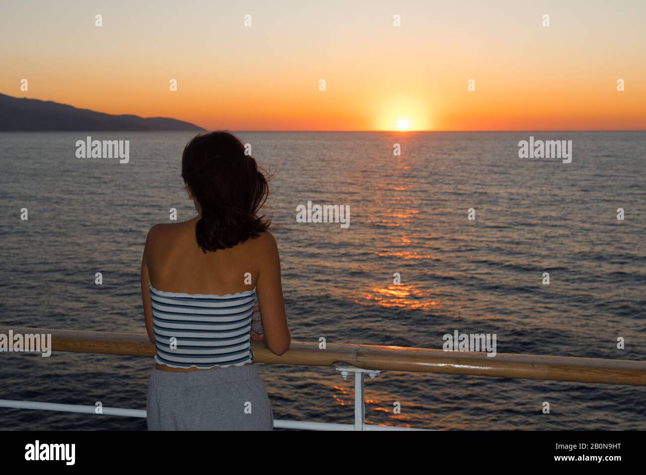 Un adolescent asiatique en métro se tenant sur la terrasse du ferry en regardant le coucher du soleil sur le ferry à destination de Lesvos Banque D'Images
