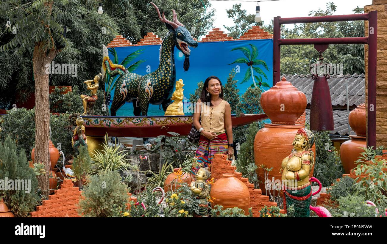 Femme dans le sarong debout dans le jardin wat et entouré de statues et de plantes dans Pak Nam Gram, Pranburi Thaïlande Banque D'Images