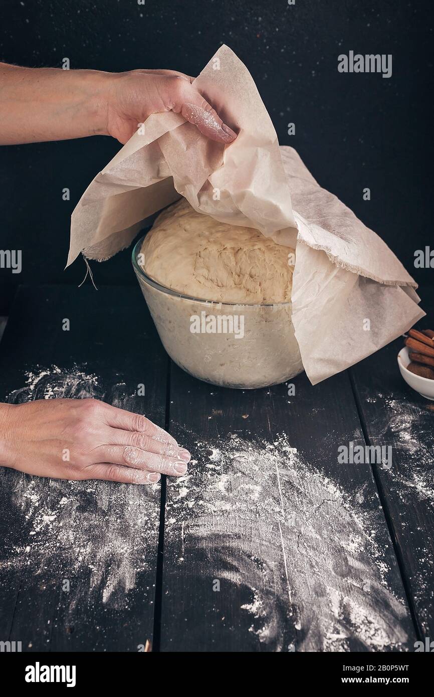 Les mains féminines tiennent une serviette sur une pâtisserie fermentée maison pour les petits pains. Prise de vue verticale. Recette étape par étape Banque D'Images