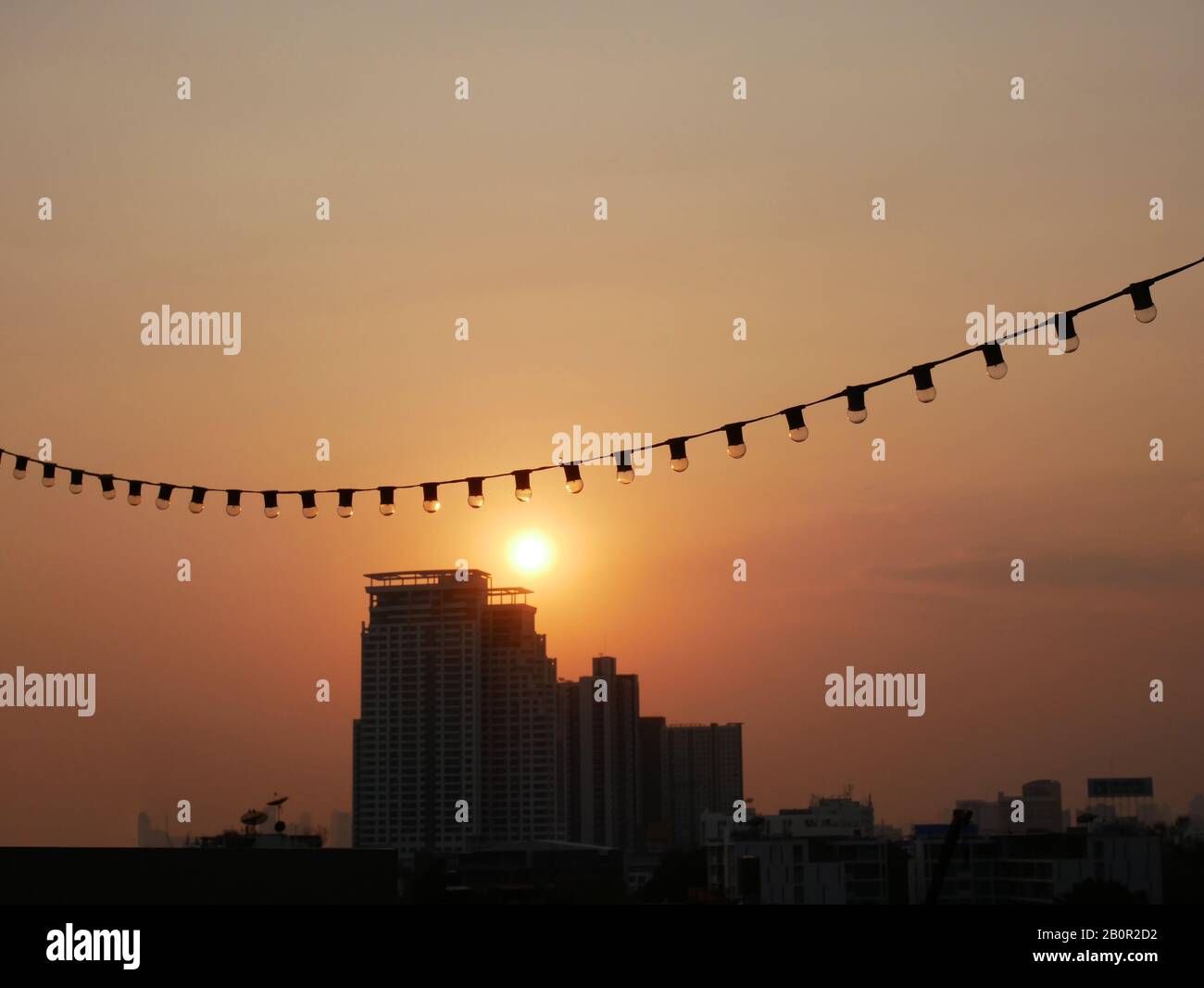 Vue sur la ville de Bangkok depuis le bâtiment situé sur le toit au crépuscule avant le coucher du soleil avec fil électrique à bulbe suspendu au premier plan. Image du coucher de soleil dans la ville Banque D'Images