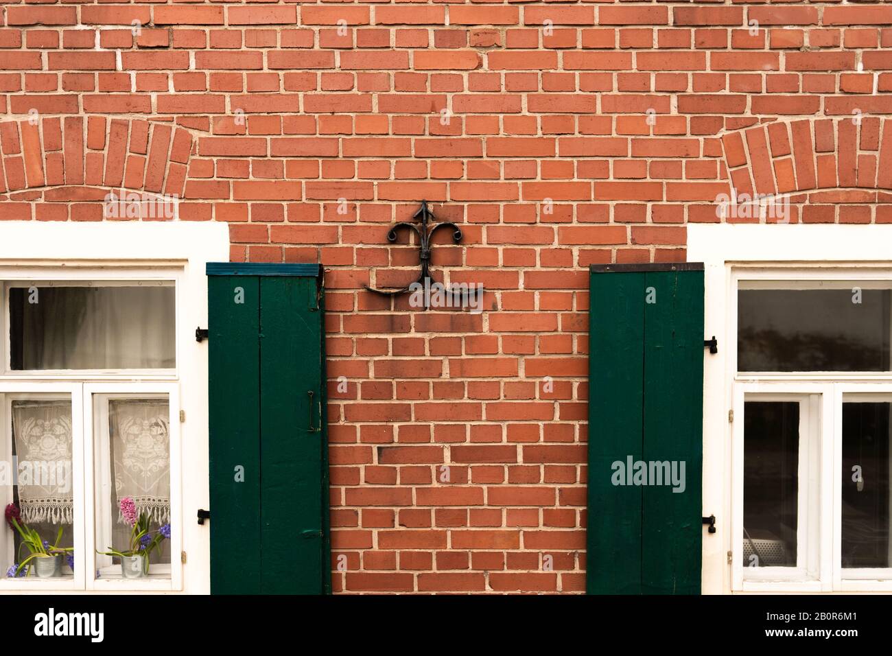 Mur de briques d'une maison avec fenêtres et volets verts Banque D'Images