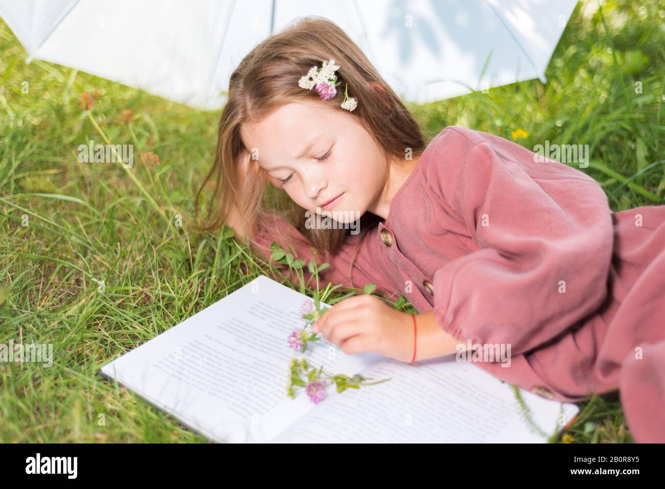 Petite fille mignonne est livre de lecture. Enfant avec des fleurs sur l'herbe verte Banque D'Images