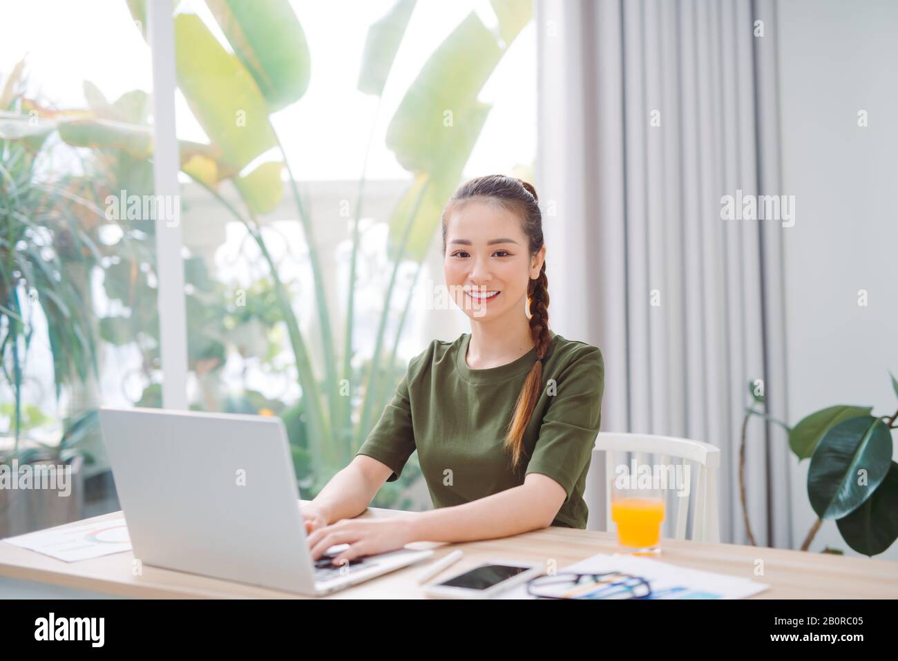 femme assise à la table à la maison travaillant à l'aide d'un ordinateur portable avec un visage heureux debout et souriant avec un sourire confiant montrant les dents Banque D'Images