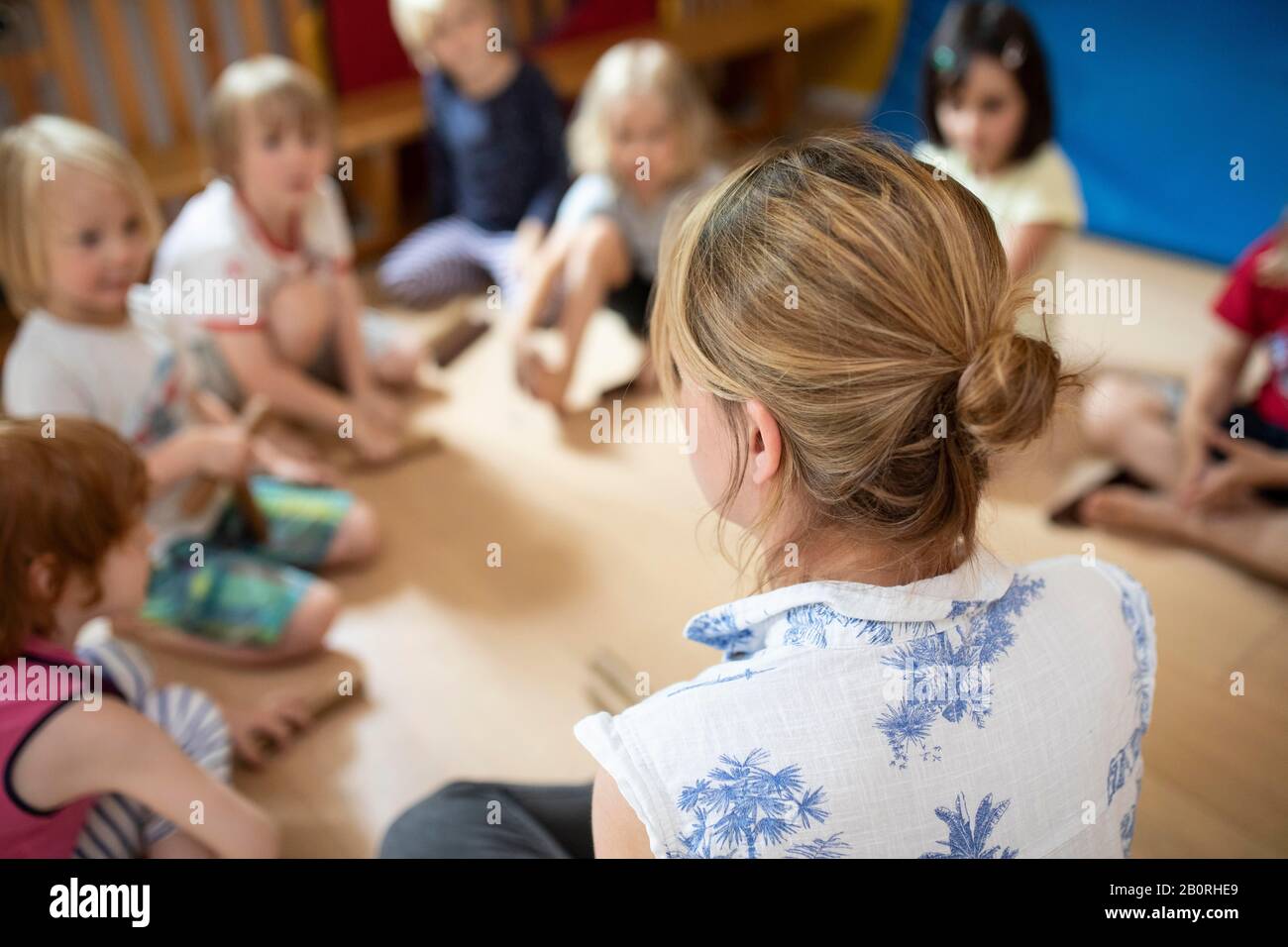 Éducateur assis dans une école maternelle avec des enfants dans un cercle et fait des jeux, Cologne, Rhénanie-du-Nord-Westphalie, Allemagne Banque D'Images