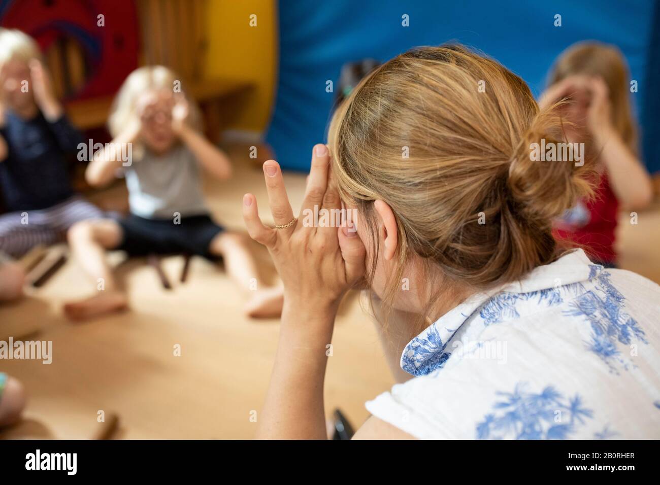 Éducateur assis dans une école maternelle avec des enfants dans un cercle et fait des jeux, Cologne, Rhénanie-du-Nord-Westphalie, Allemagne Banque D'Images