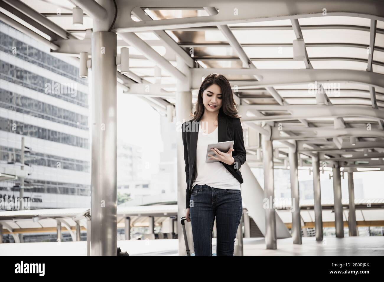 Belle jeune femme d'affaires marchant à l'extérieur de la station de transport en commun. Voyageur d'affaires avec valise sur le chemin de l'aéroport. Banque D'Images