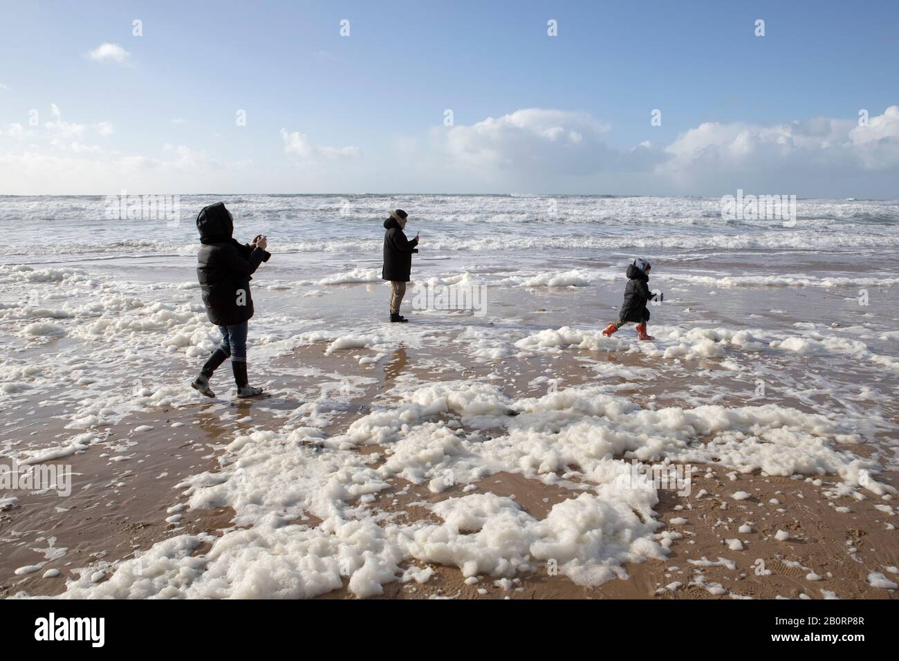 Une famille s'amuse dans la mousse de mer fouettée à Watergate Bay, Cornwall par de forts vents de l'ouest et la haute mer Banque D'Images
