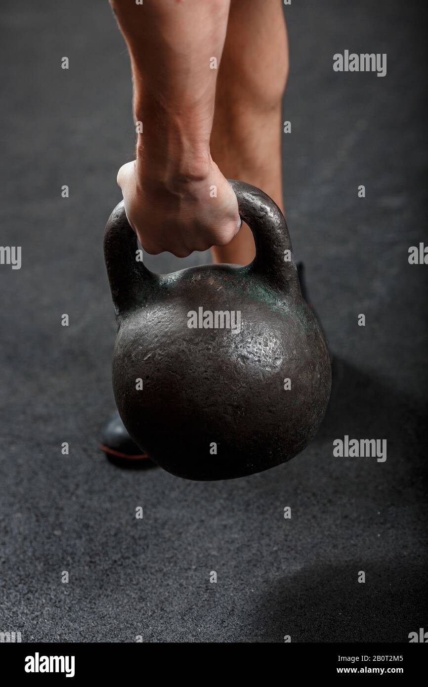 Une partie de la main de l'homme ald jambe, faisant l'exercice de culturisme, soulevant noir gymnastique kettlebell Banque D'Images