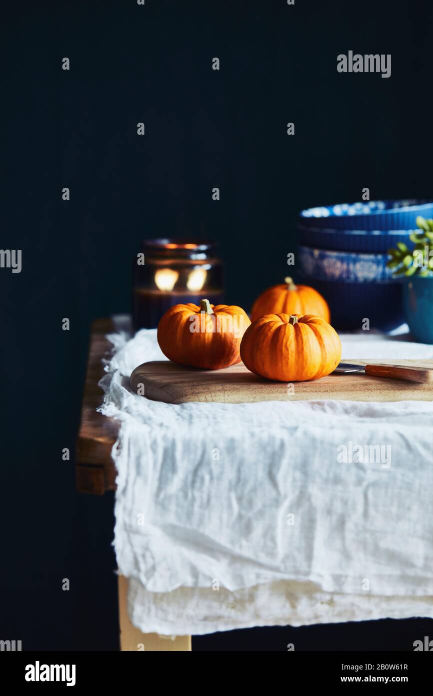 Toujours la vie avec des citrouilles orange sur une table en bois avec une nappe blanche et un fond noir. Banque D'Images