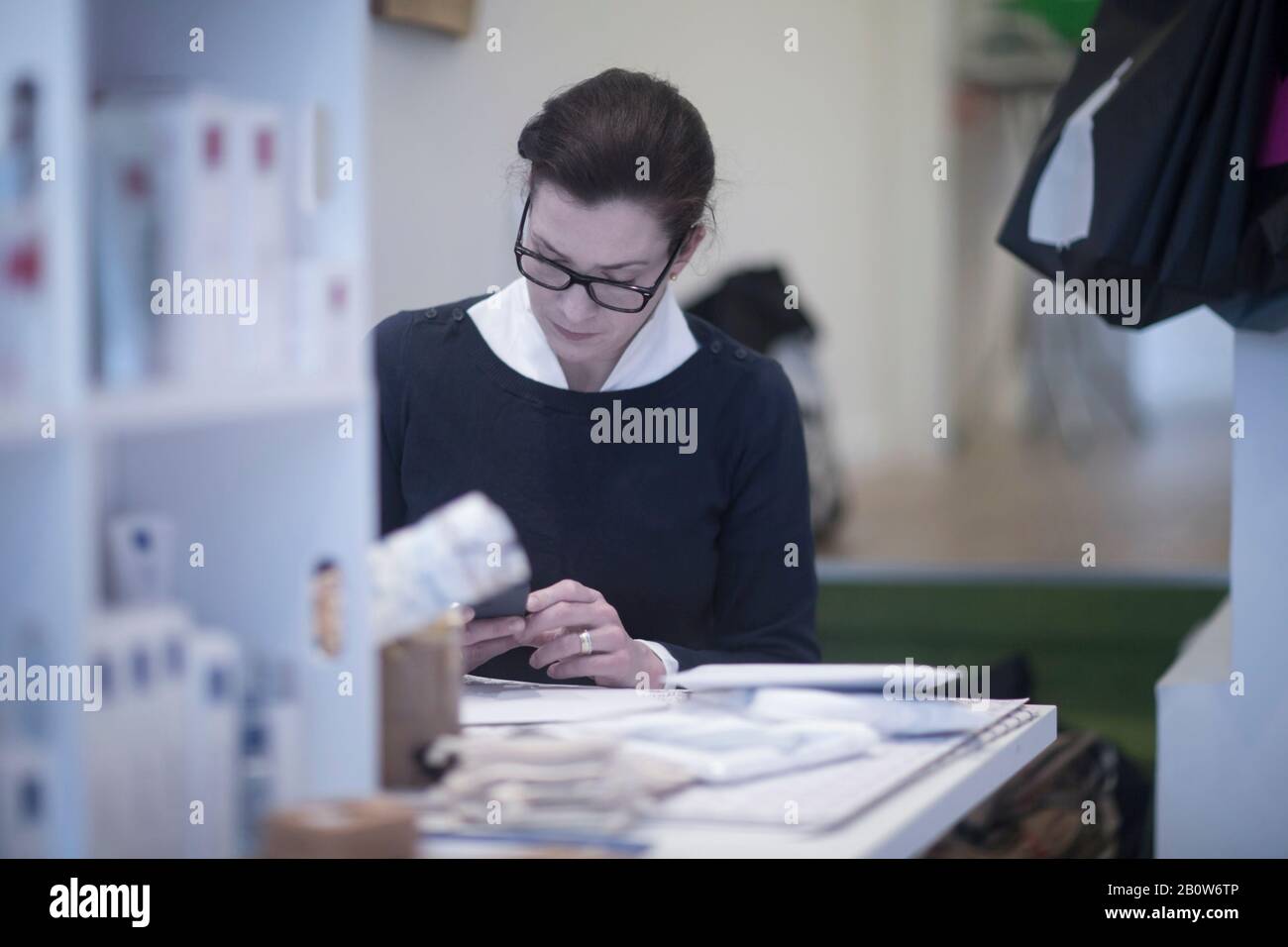 Lunettes de port sur mesure pour femme, assise à la table, pour vérifier son téléphone portable. Banque D'Images