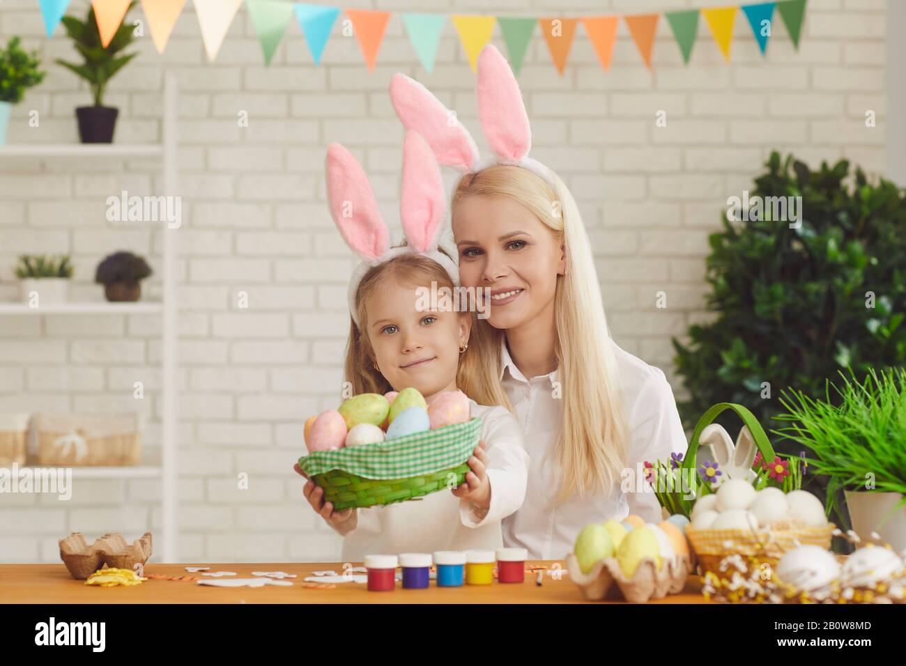 Joyeuses pâques. La fille et la mère aux oreilles de lapin décorent les œufs de Pâques assis à une table Banque D'Images