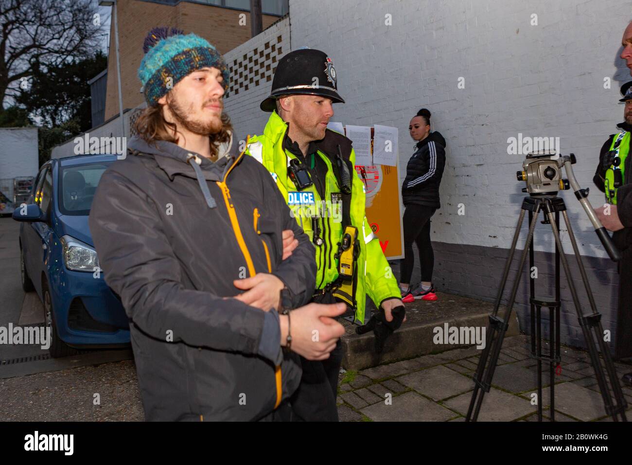 Cambridge, Royaume-Uni. 21 février 2020. Un policier escorte un militant de la rébellion d'extinction en détention devant le garage Shell SELECT sur Newnham Road, Cambridge. L’arrestation a eu lieu lors d’une manifestation climatique ciblant les infrastructures de combustibles fossiles. Un appareil monté sur trépied et d'autres officiers sont visibles à proximité. Penelope Barritt/Alamy Live News Banque D'Images