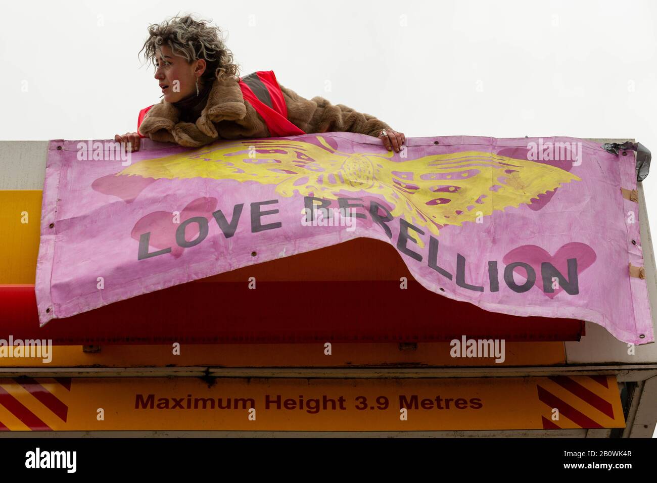 Cambridge, Royaume-Uni. 21 février 2020. Un activiste de l'extinction Rebellion affiche une bannière rose indiquant « LOVE REBELLION » avec un motif papillon jaune sur le toit du garage Shell sur Newnham Road, Cambridge. La manifestation cible les infrastructures de combustibles fossiles et promeut la justice climatique. Penelope Barritt/Alamy Live News Banque D'Images