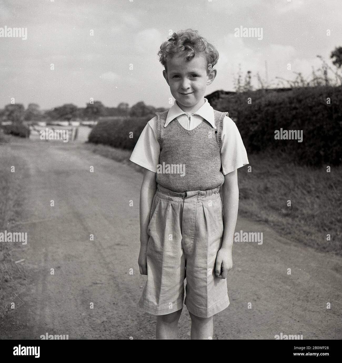 Années 1950, historique, un jeune garçon portant une chemise à manches courtes avec col zippé, débardeur et short long debout pour une photo sur un chemin de campagne, Angleterre, Royaume-Uni. Banque D'Images