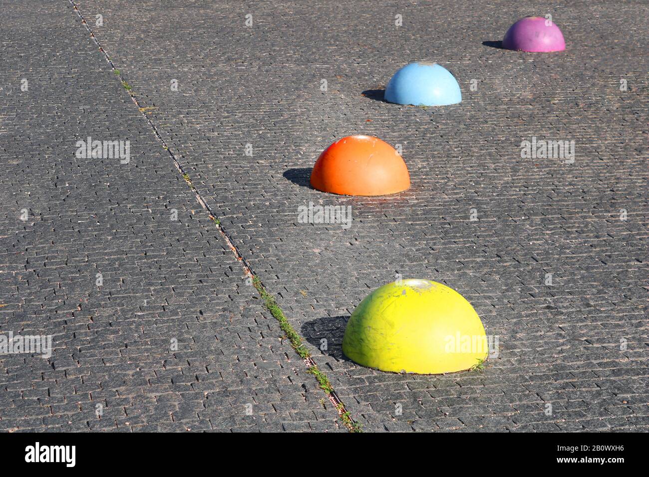 Hémisphères multicolorés en béton limitant l'entrée des voitures et de la rue pavée Banque D'Images