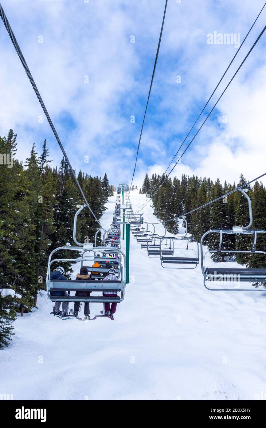 Les skieurs et planchistes non identifiables sur télésiège remontant une pente de ski dans la montagne enneigée (éventail des Rocheuses canadiennes. Banque D'Images