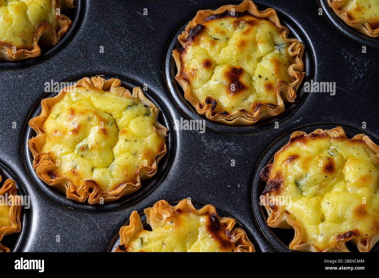 Tasses à pâtisserie filo remplies de mélange de fromage feta dans une poêle à pâtisserie cupcake. Banque D'Images
