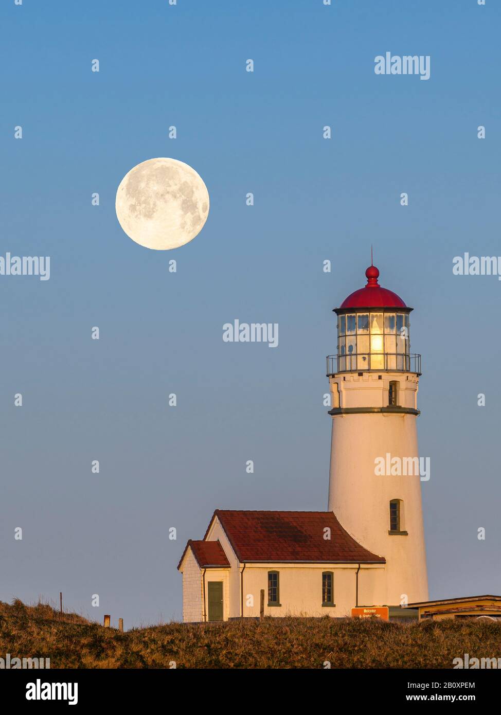 Phare du Cap Blanco au lever du soleil avec une « Lune de neige » comme ensemble pleine lune; parc national du Cap Blanco, côte sud de l'Oregon. (Photo composite de la lune an Banque D'Images