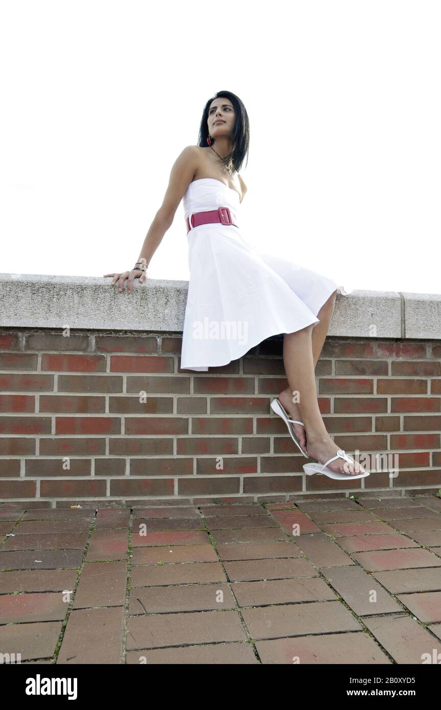Jeune femme avec robe blanche assise sur un mur de briques, Banque D'Images