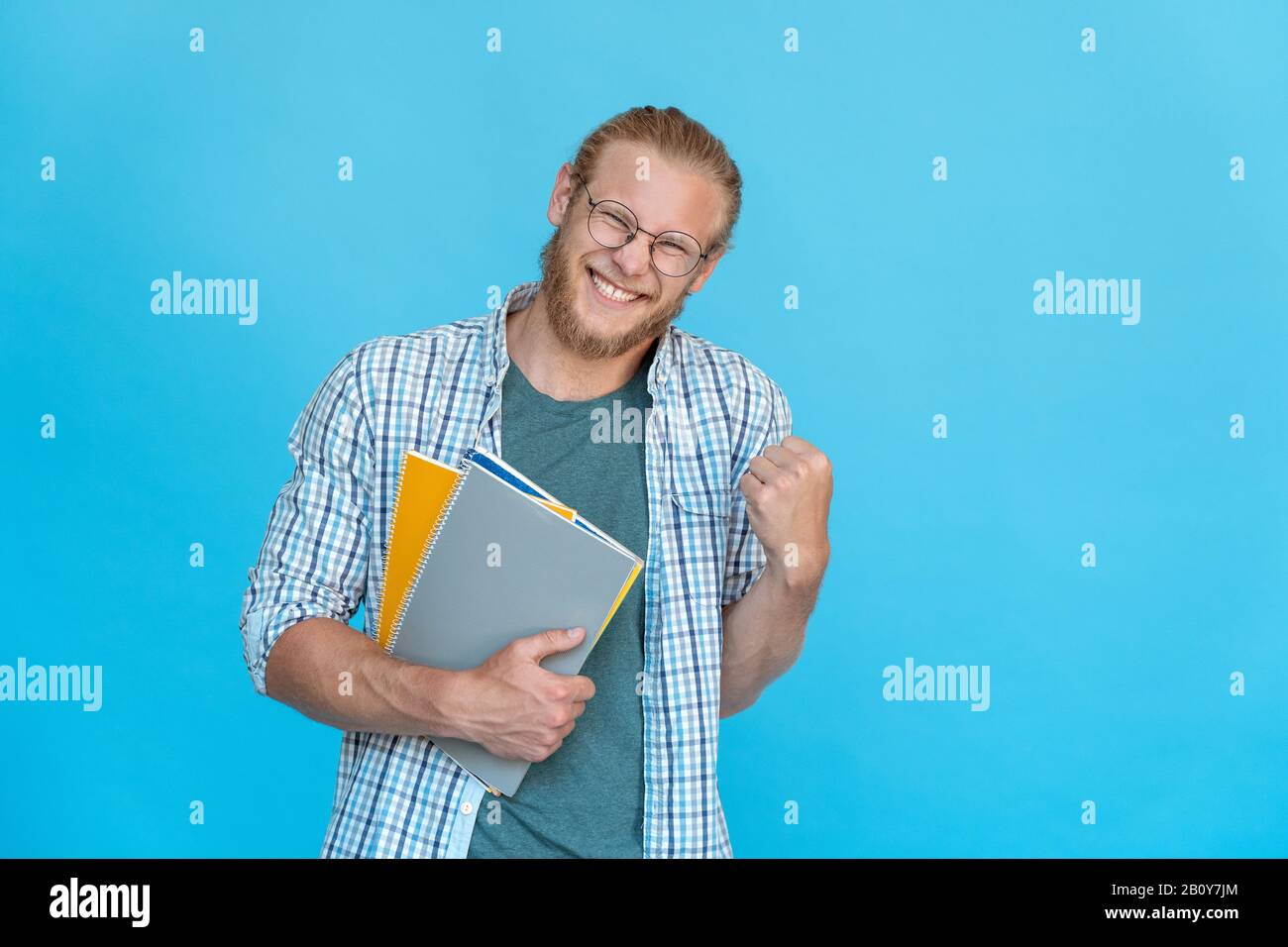 Un étudiant heureux et heureux barbu dans des lunettes tient des copybooks oui geste de victoire Banque D'Images
