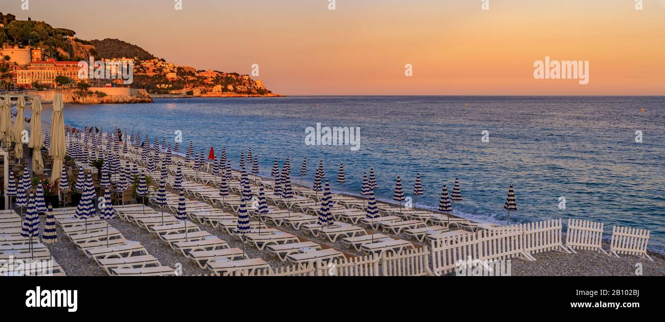Coucher de soleil sur la plage par la célèbre Promenade des Anglais avec chaises longues, parasols et la mer Méditerranée en arrière-plan à Nice, au sud de la France Banque D'Images
