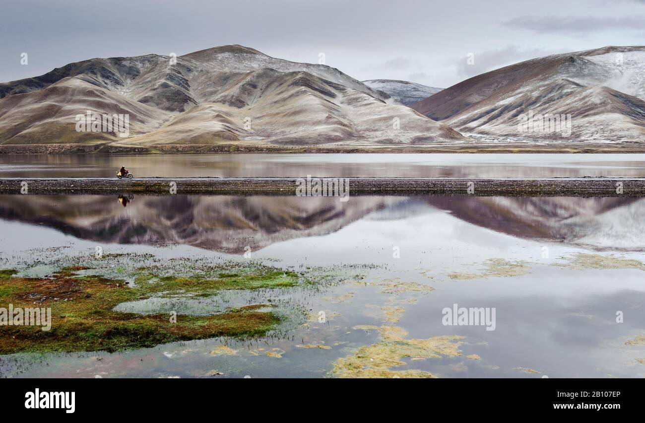 Le moine tibétain passe devant un réservoir près de Sershul, Kham, Tibet après une tempête de neige sur une moto Banque D'Images