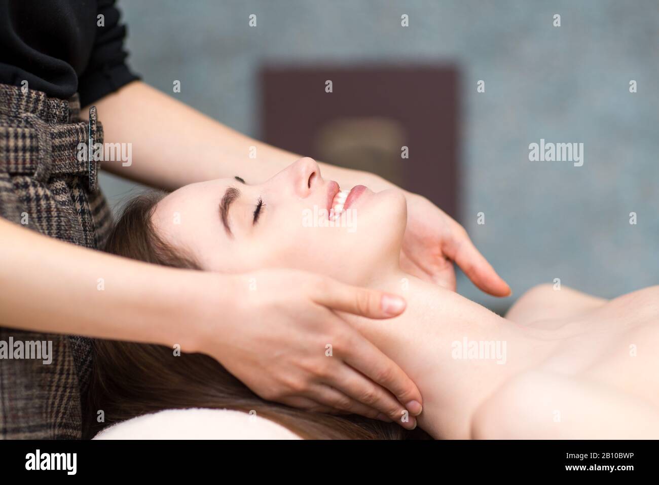 Jeune femme souriante souriante recevant un massage du visage de la tête dans un spa de beauté Banque D'Images