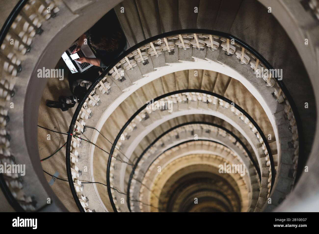 Faible profondeur de champ (foyer sélectif) image avec une femme journaliste utilisant son ordinateur portable et téléphone mobile sur un escalier en spirale très profond Banque D'Images