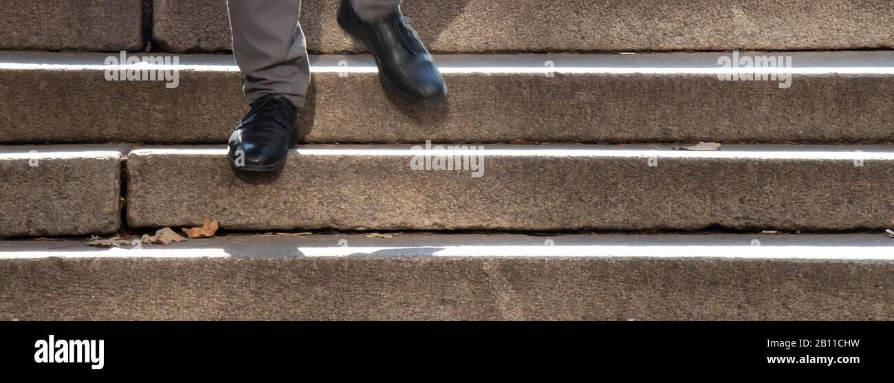 Un homme en chaussures noires marchant dans l'escalier extérieur public, détail de ses pieds dans le flou de mouvement Banque D'Images