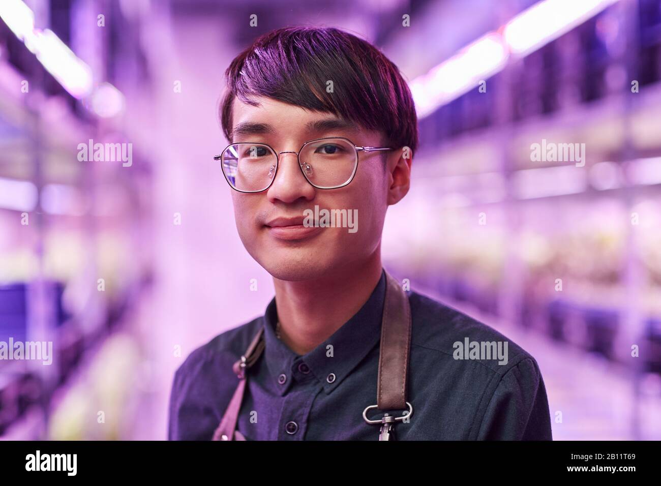 Portrait du jeune homme asiatique dans des lunettes regardant la caméra tout en se tenant dans l'usine Banque D'Images