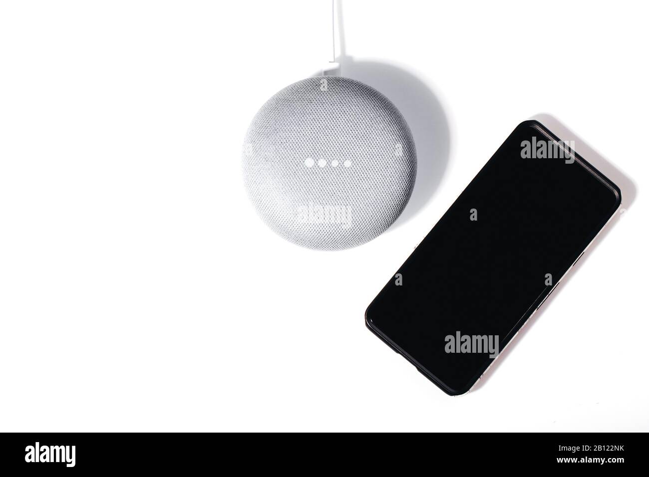Concept d'assistant numérique. Enceinte plate avec éclairage LED activé et smartphone isolé sur fond blanc. Banque D'Images