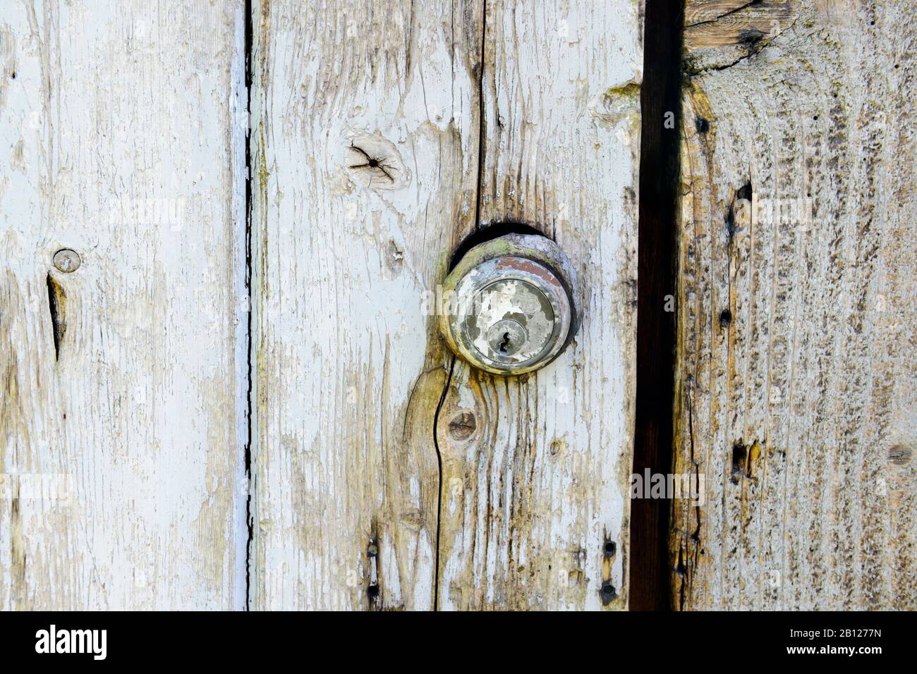 Ancienne serrure de cylindre Yale dans une porte en bois peinte et dépeinte, réutilisée comme porte de hangar de poulet. Banque D'Images