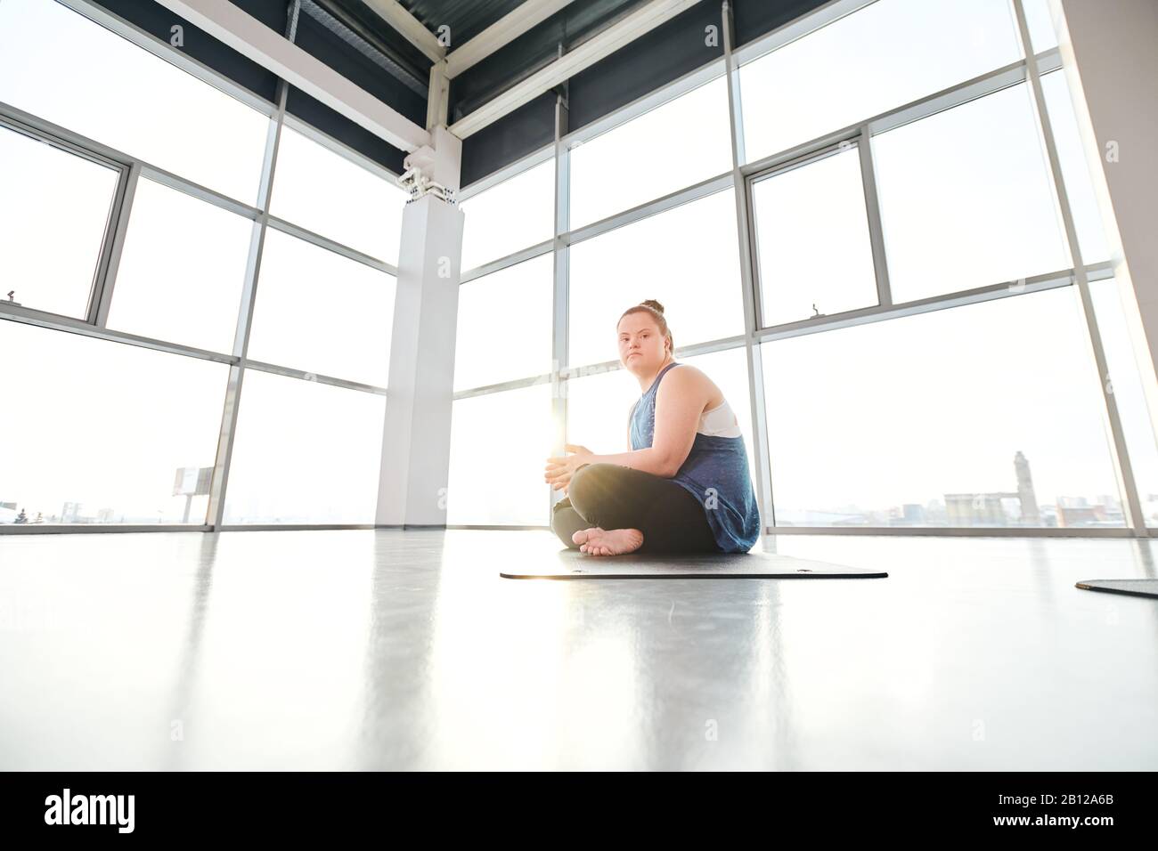 Jeune femme disable avec jambes croisées faisant de l'exercice de yoga sur tapis dans la salle de gym Banque D'Images