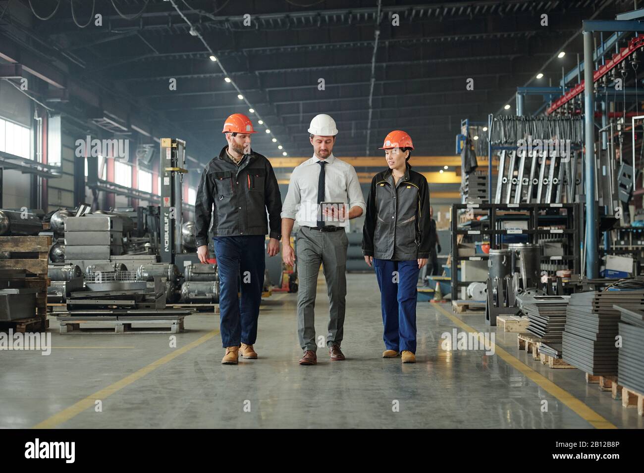 Groupe de travailleurs contemporains de l'usine dans les casques discutant des données techniques Banque D'Images