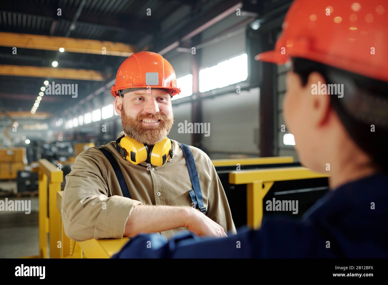 Joyeux jeune ingénieur barbu dans un casque sans tête parlant à son collègue Banque D'Images