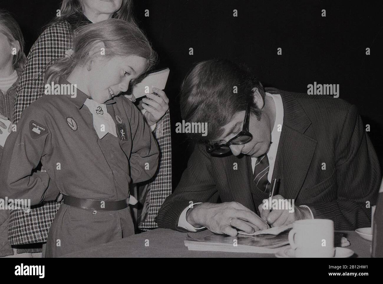 1960, historique, présentateur et animateur de télévision britannique, Leslie Crowther à une œuvre de bienfaisance qui signe un autographe pour un jeune brownie ou guide de fille, Londres, Angleterre, Royaume-Uni. Un animateur populaire, en particulier avec les jeunes, Crowther était bien connu comme le présentateur du célèbre programme 'Crackerjack' pour enfants et sur BBC radio One, 'Junior Choice'. Il a également présenté « Mes enfants », un programme de Noël sur le service hospitalier pour enfants. Banque D'Images