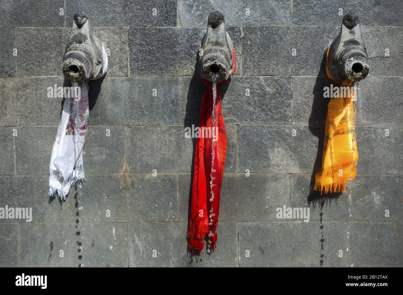 Fontaine d'eau avec rangée De Trois Tuyaux en pierre texturée mur enveloppé de Scarfs colorés avec texte qui lit "le Népal est un pays multiculturel" Banque D'Images