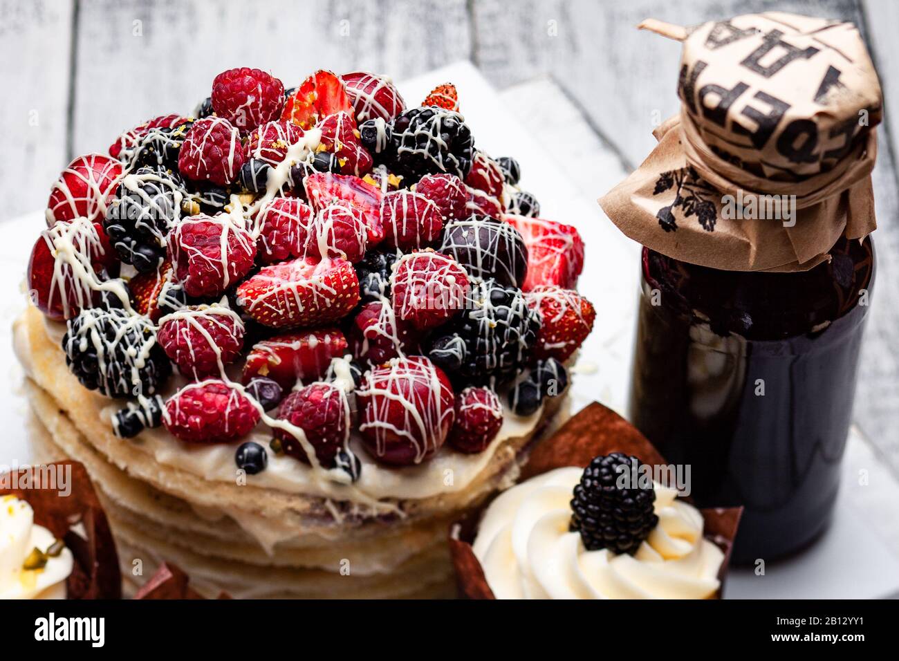 Gâteau aux crêpes avec une casquette de baies trempées dans du chocolat blanc sur une table en bois blanc avec quelques muffins belges et une bouteille de sirop Banque D'Images