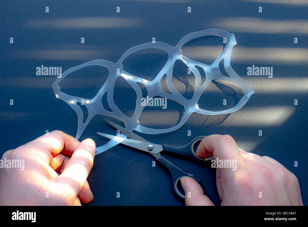 Une personne coupant un paquet de six anneaux ou six chapes de paquet avec des ciseaux Banque D'Images