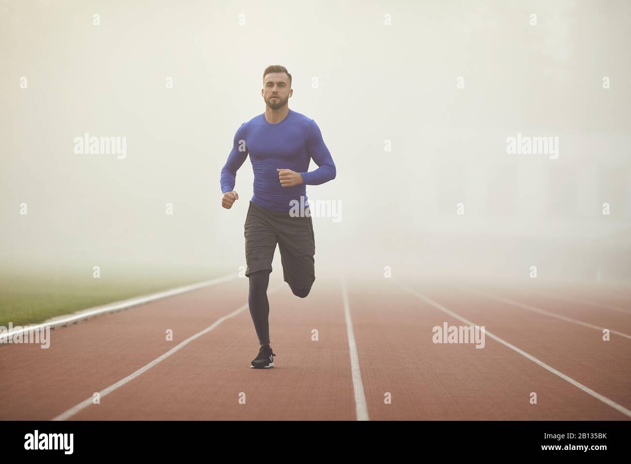 Un jeune athlète exécute sur un stade dans le brouillard. Banque D'Images