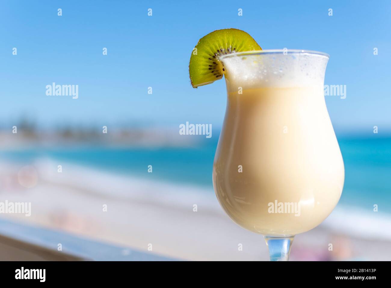 Une boisson alcoolisée glacée mélangée avec une tranche de kiwi fraîche sur le bord devant une plage tropicale et la mer. Mise au point sélective sur le kiwi. Banque D'Images