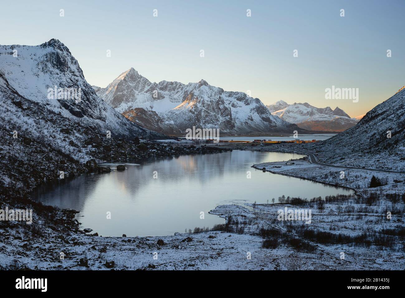 Lac gelé reflète les sommets ensoleillés des montagnes en arrière-plan, Lofoten, Nordland, Norvège Banque D'Images