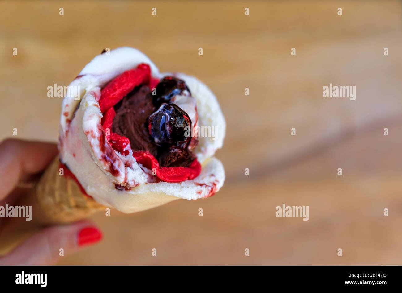 Femme tenant une glace en forme de rose avec de l'amarena, du chocolat et de la fraise avec une cerise sur le dessus dans un cône de sucre à Nice, France Banque D'Images