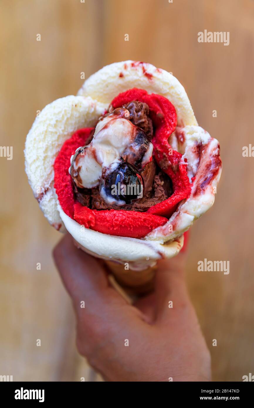Femme tenant une glace en forme de rose avec de l'amarena, du chocolat et de la fraise avec une cerise sur le dessus dans un cône de sucre à Nice, France Banque D'Images
