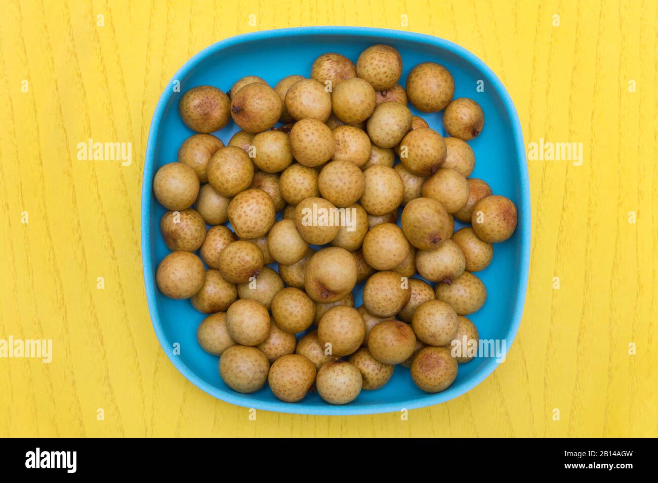 longan frais dans un bol bleu sur une table jaune Banque D'Images