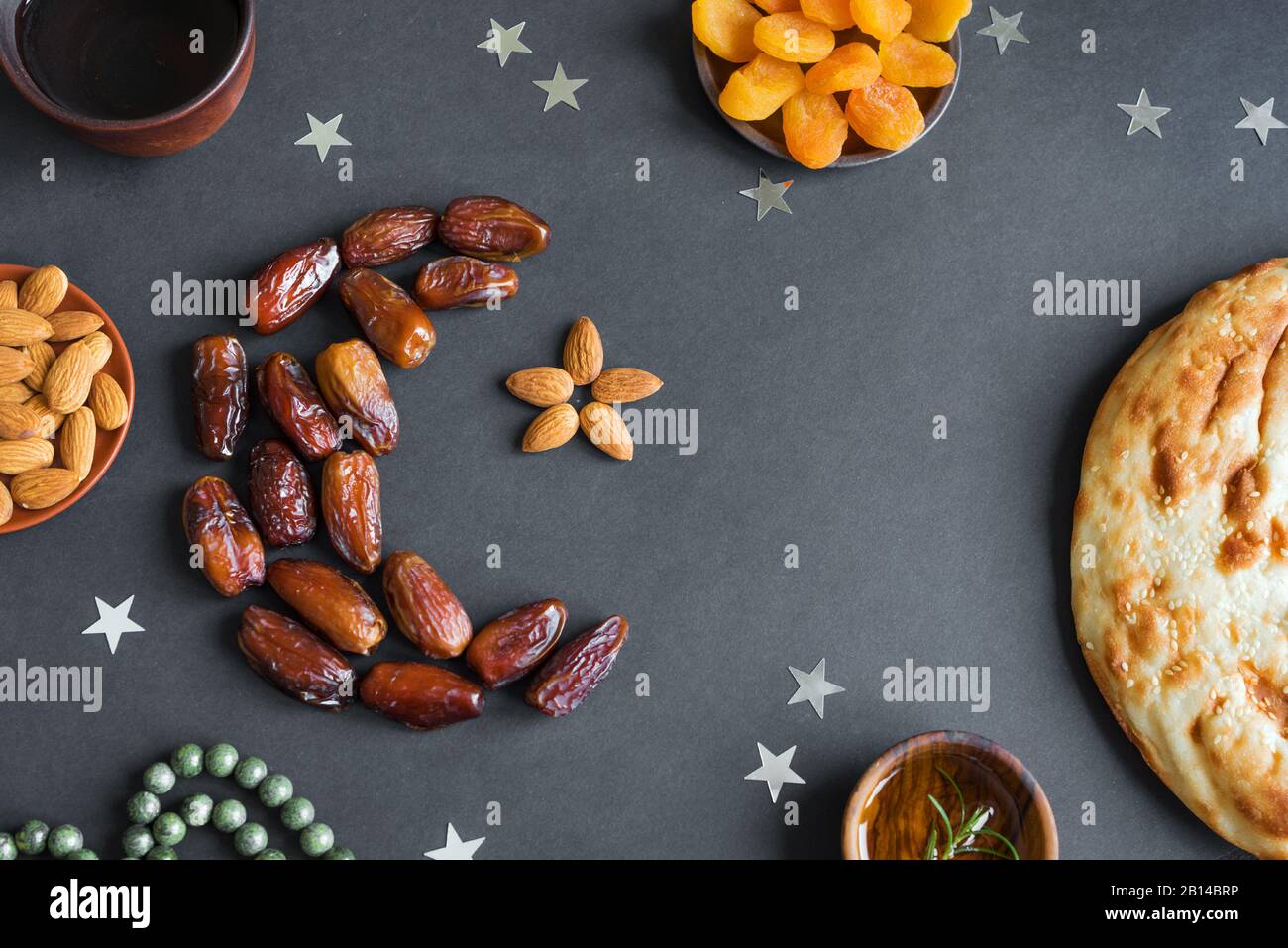 Ramadan Kareem musulman avec dates fruits disposés en forme de croissant de lune, eau et pain sur fond noir, vue de dessus. Nourriture iftar ou fête Iftar c Banque D'Images