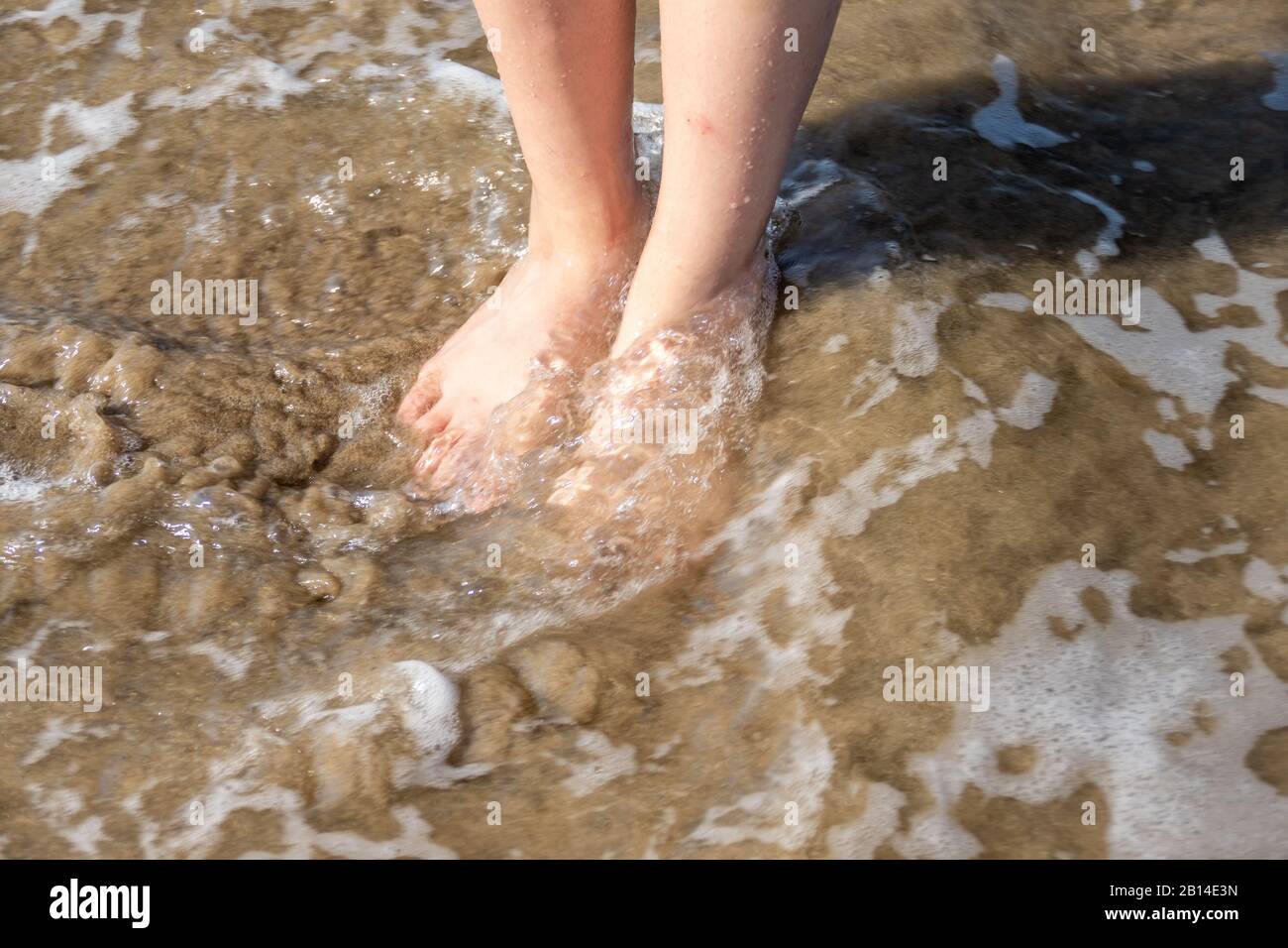 Pieds de jeune fille dans l'eau de mer et le sable à la plage Banque D'Images