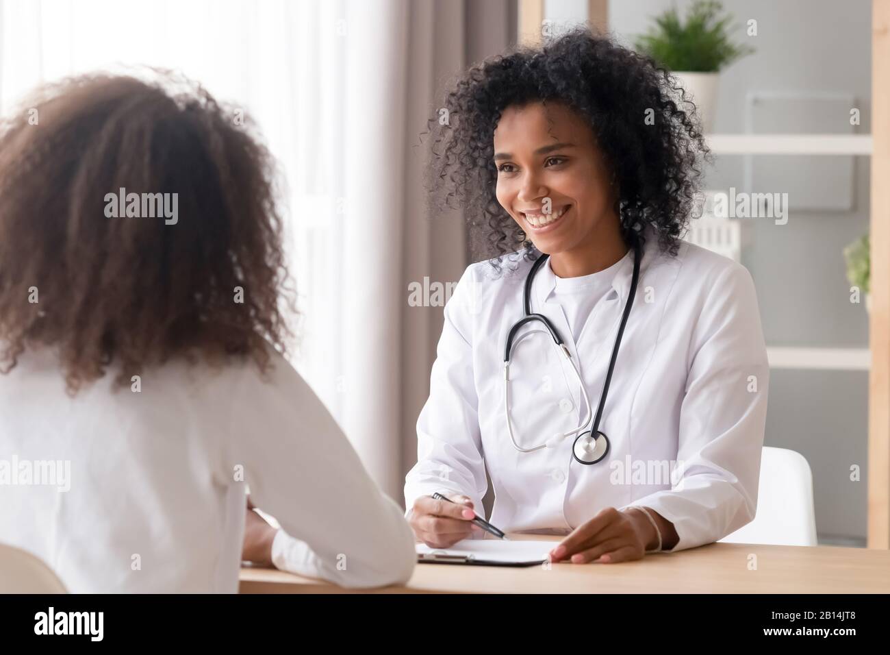 Sourire femme africaine médecin parlant à l'adolescence patient prendre des notes Banque D'Images