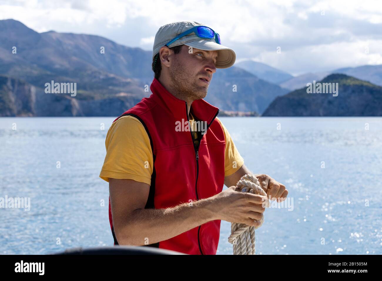 Un homme sur un yacht nouent un nœud sur une corde, portant un jaune rouge, portant un capuchon et des lunettes. Banque D'Images