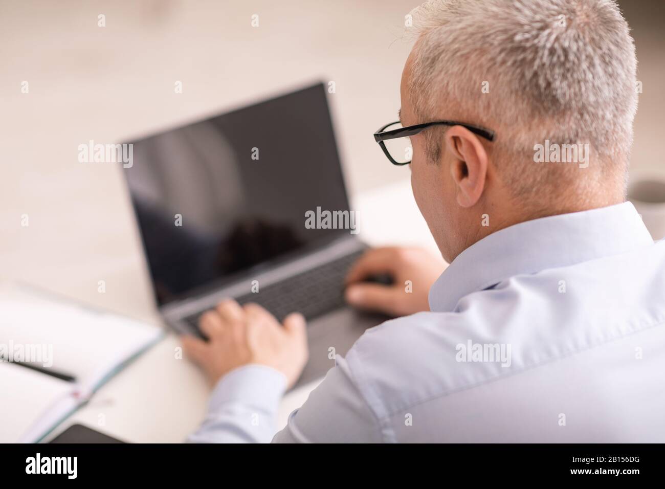 Homme senior méconnaissable utilisant un ordinateur portable au bureau Banque D'Images